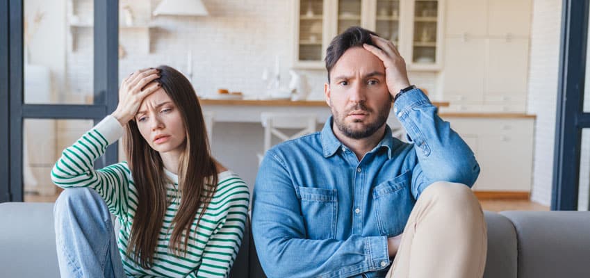 Young couple sitting next to each other on couch visibly uncomfortable.